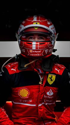 a man wearing a red racing suit and helmet with his hands on his hips in front of him