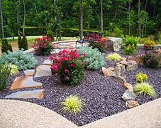 a rock garden with flowers and rocks in the middle, surrounded by trees on either side