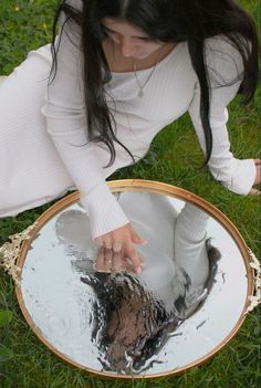 a woman kneeling down in the grass with her hand on top of a round mirror