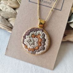 a necklace with an embroidered flower on it sitting in front of a card and box