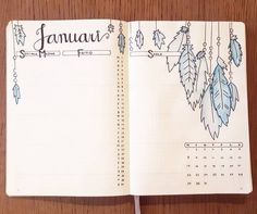 an open planner with blue feathers hanging from it's side on a wooden table