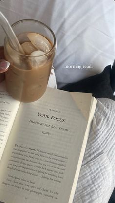 someone is reading a book and drinking a drink from a glass with ice cubes in it