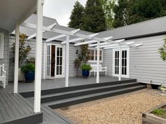 an outdoor patio with white furniture and potted plants on the side of the house