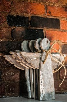 an old wooden angel with wings on it's back stands in front of a brick wall