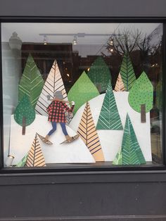 a window display with paper cut trees and snowboarders in the front, behind which is a man on skis