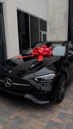 a black car with a red bow on it's hood parked in front of a building