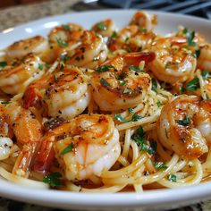 a white bowl filled with pasta and shrimp on top of a table next to a stove