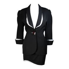 This fabulous Thierry Mugler ensemble is comprised of medium weight wool gabardine with a dramatic sculpted white lapel and cuff detail in white satin. Fitted waist has a single Tri-color abstract square button echoing the white edges of the lapels and cuffs. Medium density shoulder pads. Fitted skirt with a hidden zipper and covered satin snap at back with 3-D white detail at the hem. In overall excellent condition. There is a minute chip at the corner of the white edge of the button. Fully lined in a silk like polyester. Size 42 Please review the measurements provided to ensure a perfect fit. Jacket- Shoulders:17 inches Sleeve:20 inches Bust:38 inches Waist:29 inches Hips:40 inches Skirt- Waist:28 inches Hips: 38 inches Length: 17.25 inches White Skirt Suit, Mugler Black, Suits Outfits, Bustle Skirt, Future Clothes, Skirt Suit Set, Vintage Suits, Black And White Skirt, Blue Jumpsuits