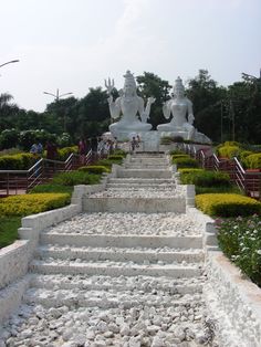 there are many steps that lead up to the buddha statues in this park, which is surrounded by flowers and bushes