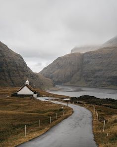 a path leading to a small house in the middle of a field with mountains behind it