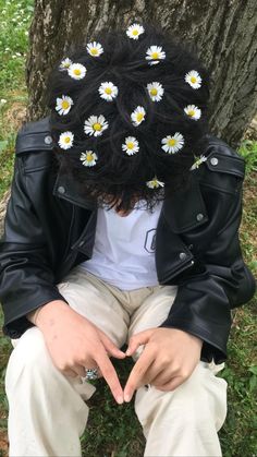 a man sitting under a tree with daisies on his head