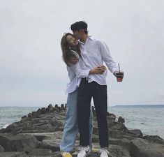 a man and woman standing on rocks by the ocean kissing while holding an object in their hand