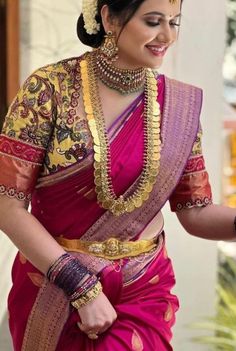 a woman in a pink and gold sari with jewelry on her head, smiling