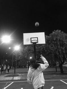 a young man is playing basketball on an outdoor court at night with the lights turned on