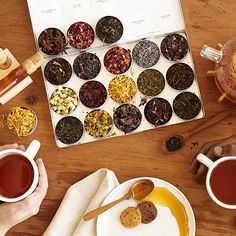 a table topped with cups and saucers filled with different types of teas next to plates