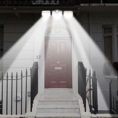 a red door is lit by two spotlights in front of a white house