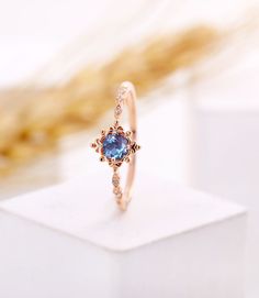 a ring with a blue stone in the center on a white surface next to a gold chain