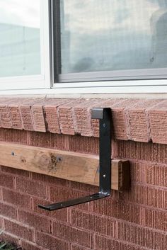 a brick wall with a black metal hook on it's side and a window in the background