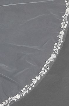 a white wedding veil with flowers and leaves on the edge is laying on top of a bed