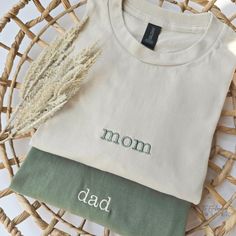 a white t - shirt with the word mom on it next to some dried plants