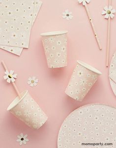 paper cups and napkins are arranged on a pink surface with daisies in the background