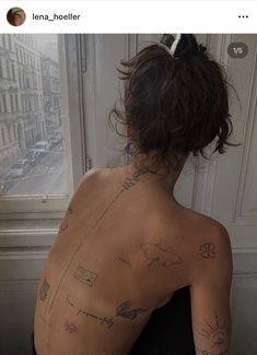 a woman with tattoos on her back looking out the window