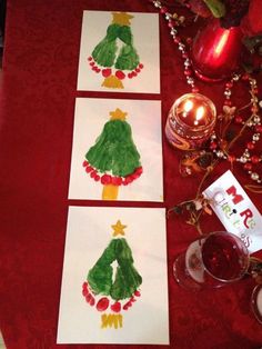 three cards with christmas trees painted on them next to a candle and some wine glasses