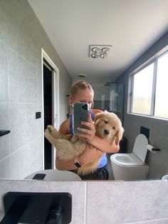 a woman is taking a selfie in the bathroom with her dog and cat on her lap