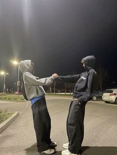 two people standing in the middle of an empty parking lot at night, one holding the other's hand