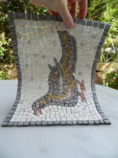 a hand is holding up a mosaic tile piece that looks like a snake on the ground