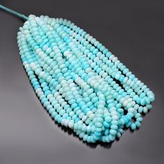 a blue beaded necklace is laying on a gray surface with a green hook in the middle