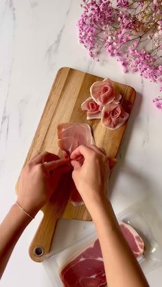 a person cutting up raw meat on top of a wooden cutting board next to flowers