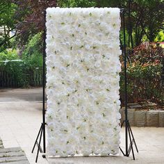 a large white flowered backdrop is set up in front of a brick walkway and trees