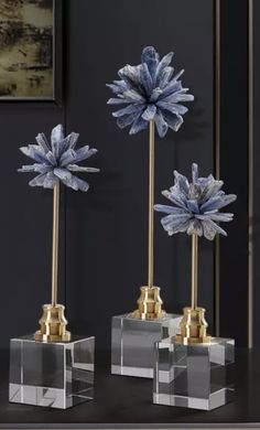 three clear vases with blue flowers in them sitting on a black table next to a painting