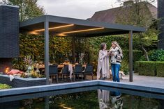 two women standing in front of an outdoor dining area next to a pond and fire pit