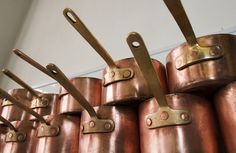 many copper colored pots are lined up on the wall with scissors hanging from each one