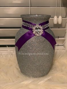 a silver vase with a purple ribbon around the bottom and a diamond brooch on it