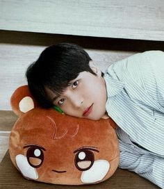 a young man laying on top of a brown bear pillow