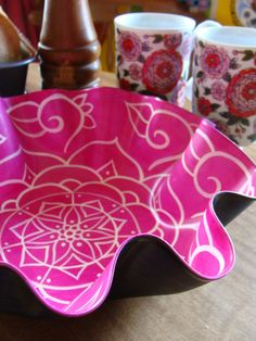 a pink and white bowl sitting on top of a table next to two coffee mugs