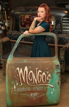 a woman with red hair and tattoos standing in an old rusty car that has writing on it