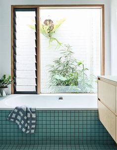 a bath tub sitting under a window next to a plant in a room with green tile