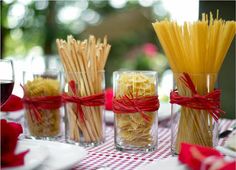 four glasses filled with different types of pasta on a red and white checkered table cloth