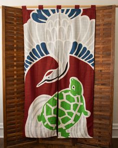 a green turtle on red and white fabric hanging from a wooden frame with bamboo shutters