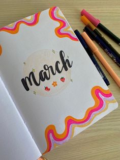 an open notebook with the word march written on it next to colored pencils and markers