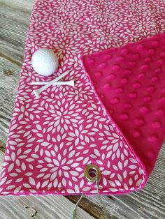 a pink and white table runner with a golf ball on it, sitting on a wooden surface