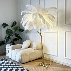 a white couch sitting next to a palm tree in a room with wooden flooring