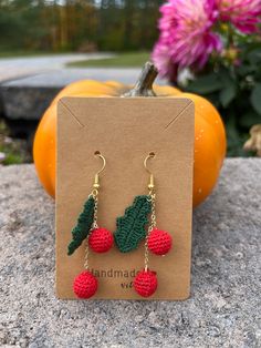 a pair of earrings with crocheted leaves and berries hanging from them on top of a card