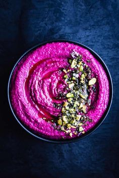 beet hummus with pistachio sauce in a black bowl on a blue background