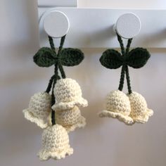 two crocheted bells hanging from a hook on a wall with leaves attached to them