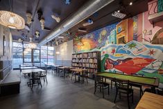 an empty restaurant with tables and chairs in front of a colorful mural on the wall